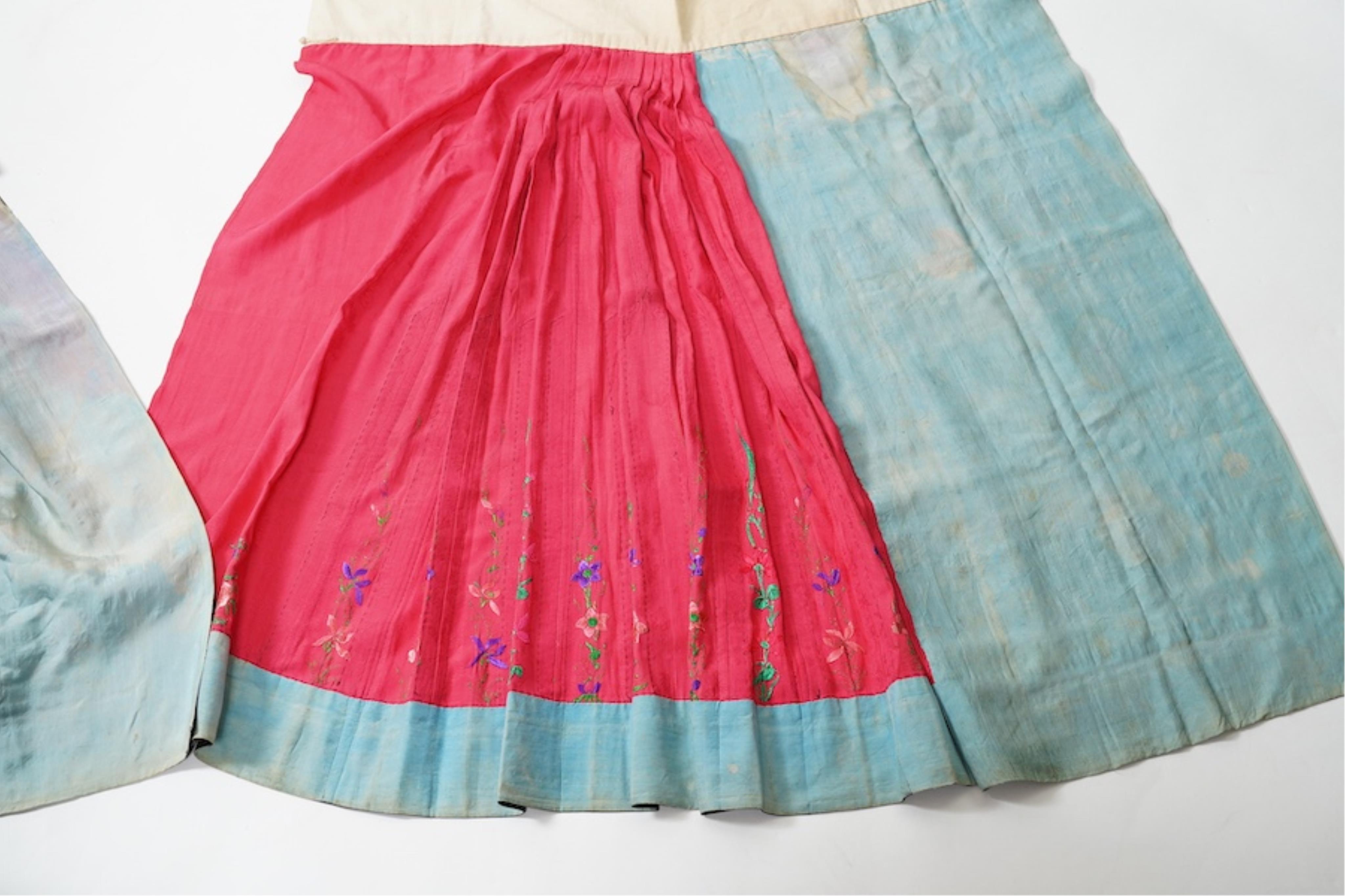Two late 19th early 20th century Chinese wedding skirts. Made with pink silk damask, embroidered with large decorative silk floral and butterfly front panels bordered by blue embroidered black silk borders between pleats